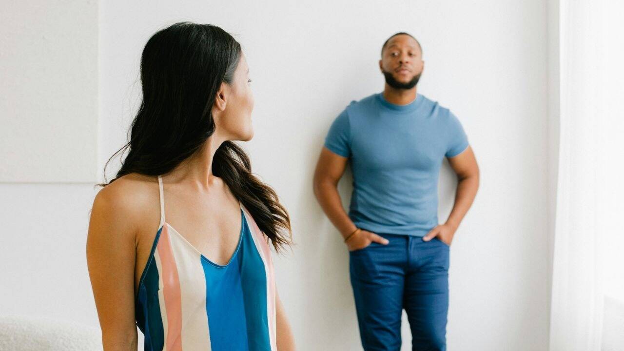 A woman in a striped top looks at a man in a blue t-shirt with a neutral expression.