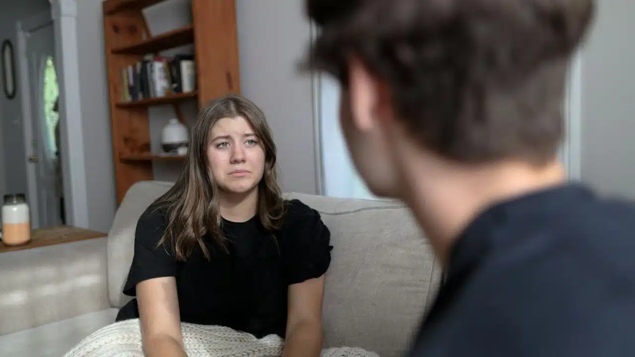 A woman with a worried expression looking at a man sitting opposite her on a couch.
