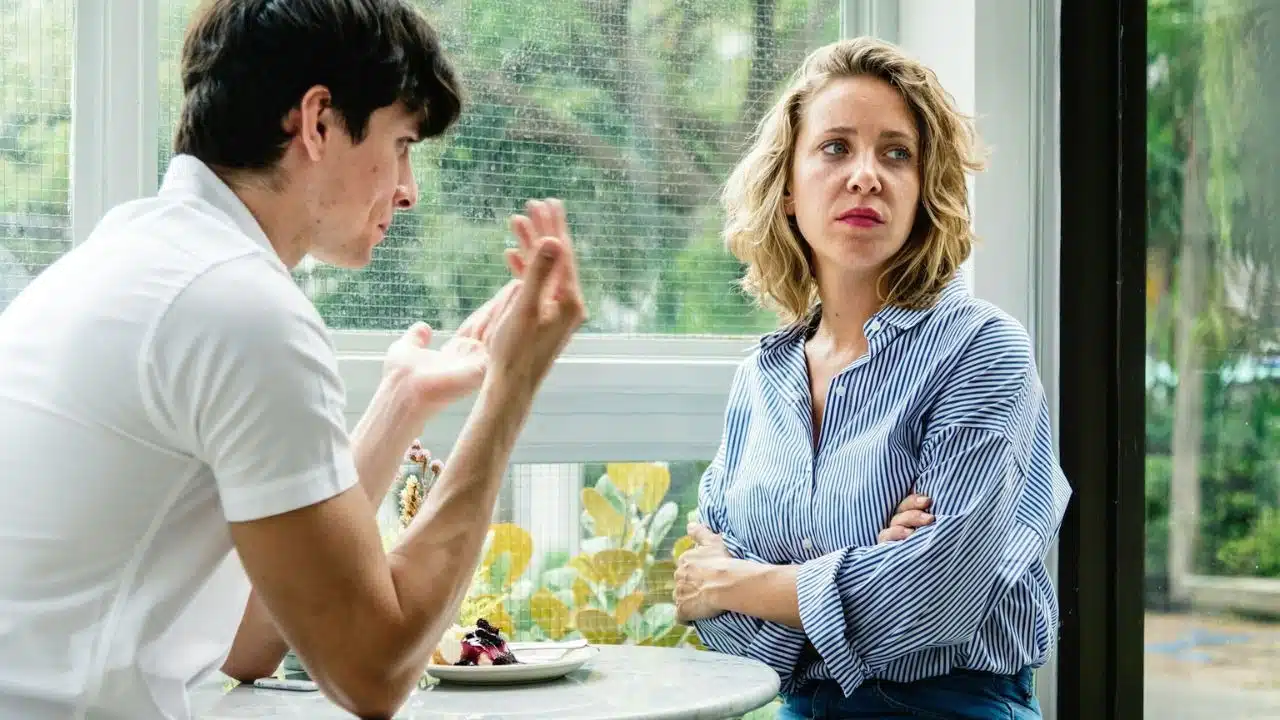 A woman with crossed arms looks annoyed at a man who is speaking to her.