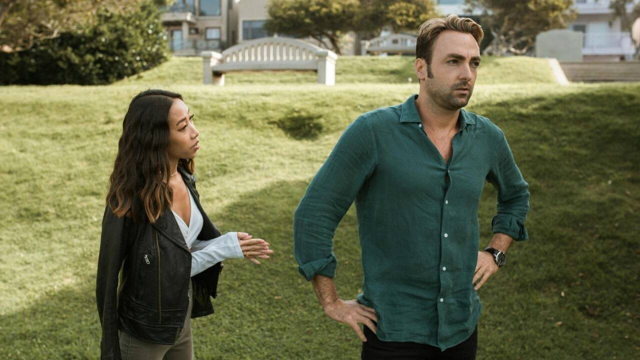 A man stands with hands on hips while a woman nearby gestures with her hands.