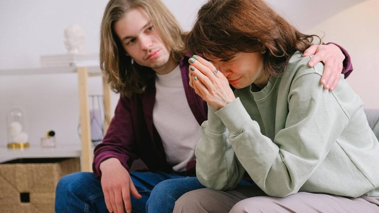 A man places a hand on the shoulder of a woman who is covering her face.