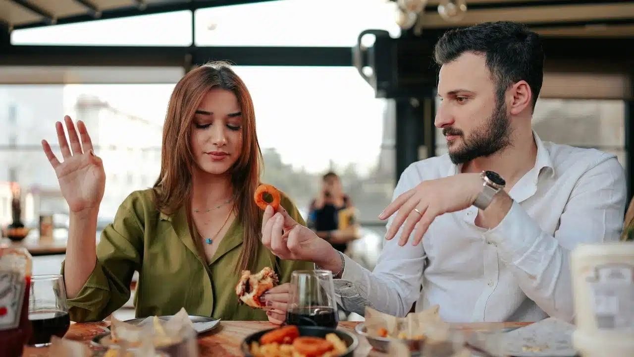 A man offers a food item to a woman who is holding up one hand.