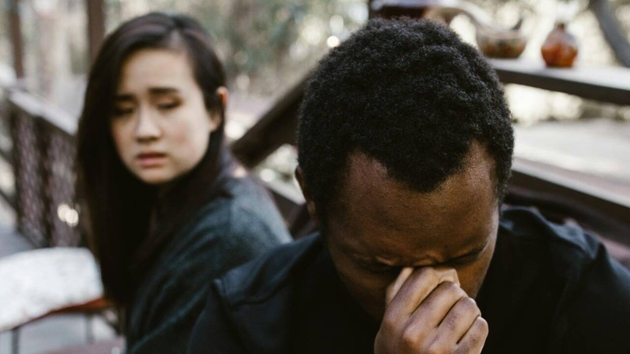 A man pinches the bridge of his nose while a woman looks at him with concern.