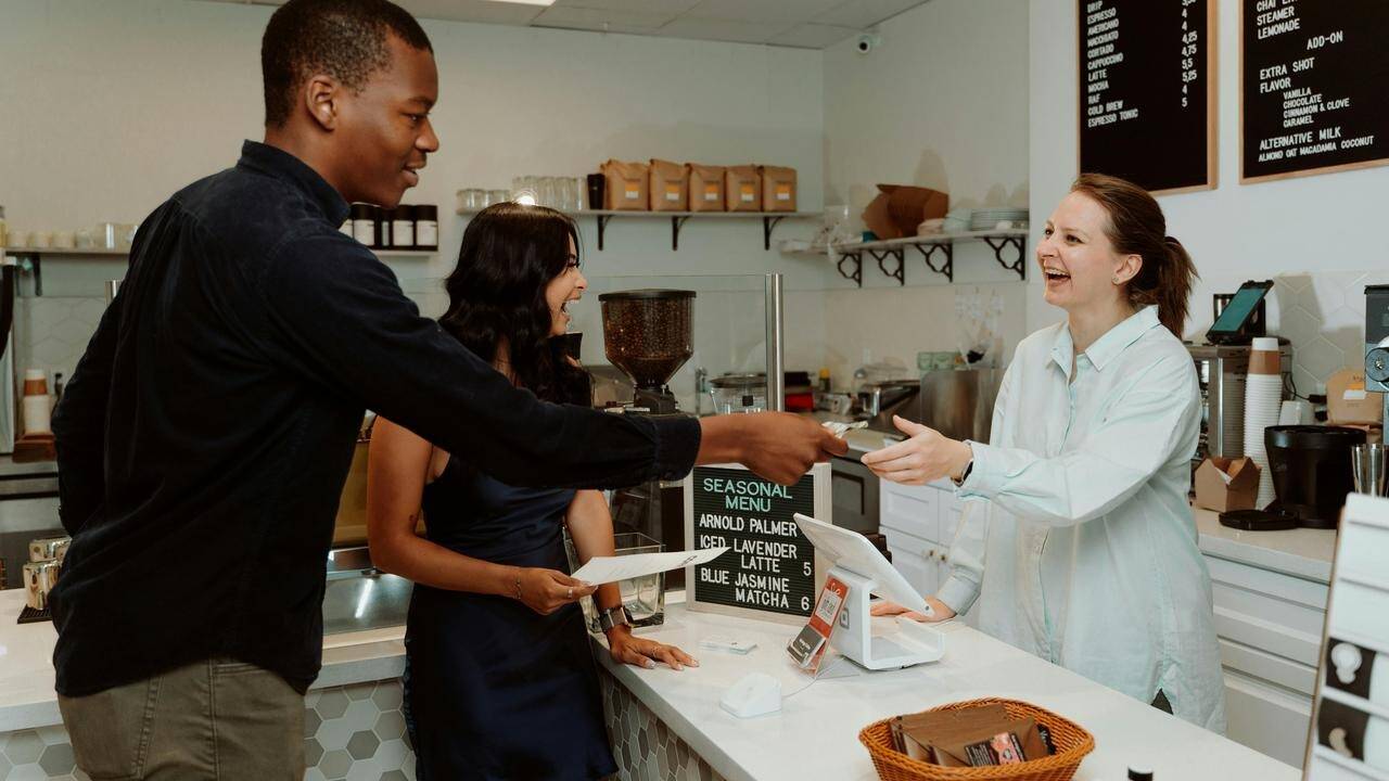A customer handing a card to a barista at a café counter while another person stands nearby.