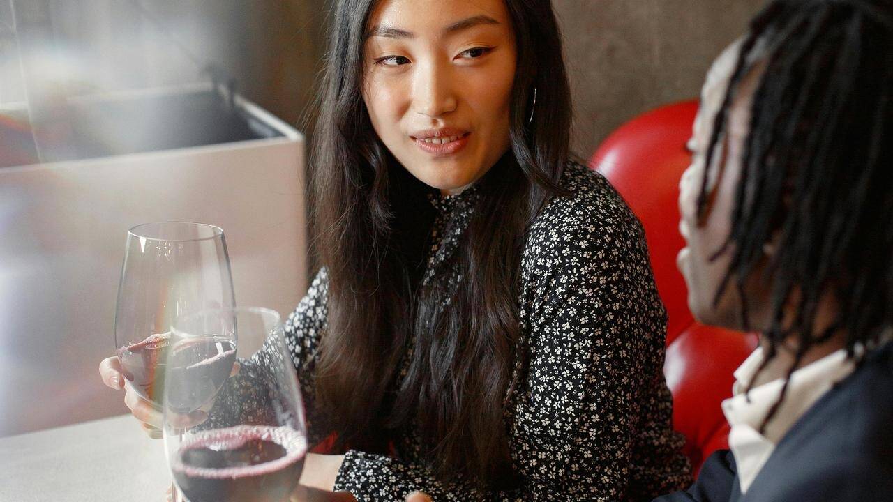 A woman holding a glass of wine while talking with another person at a table.