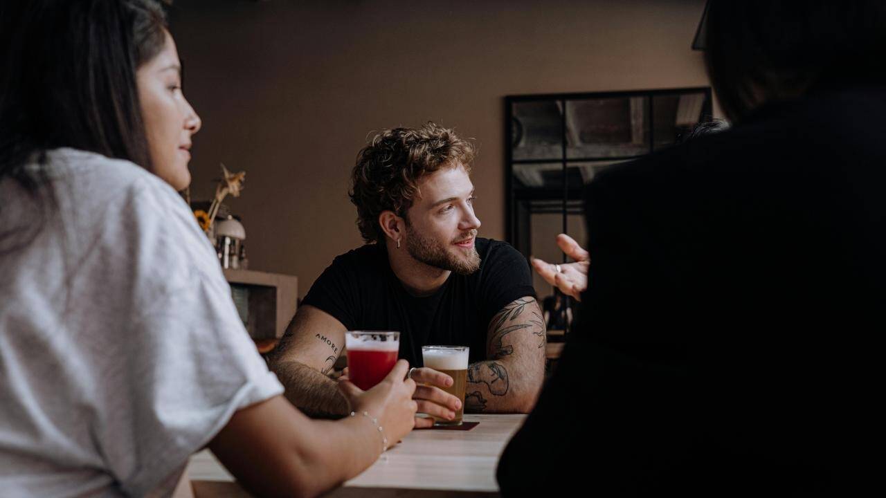 A group of people sitting at a table with drinks, talking and socializing indoors.