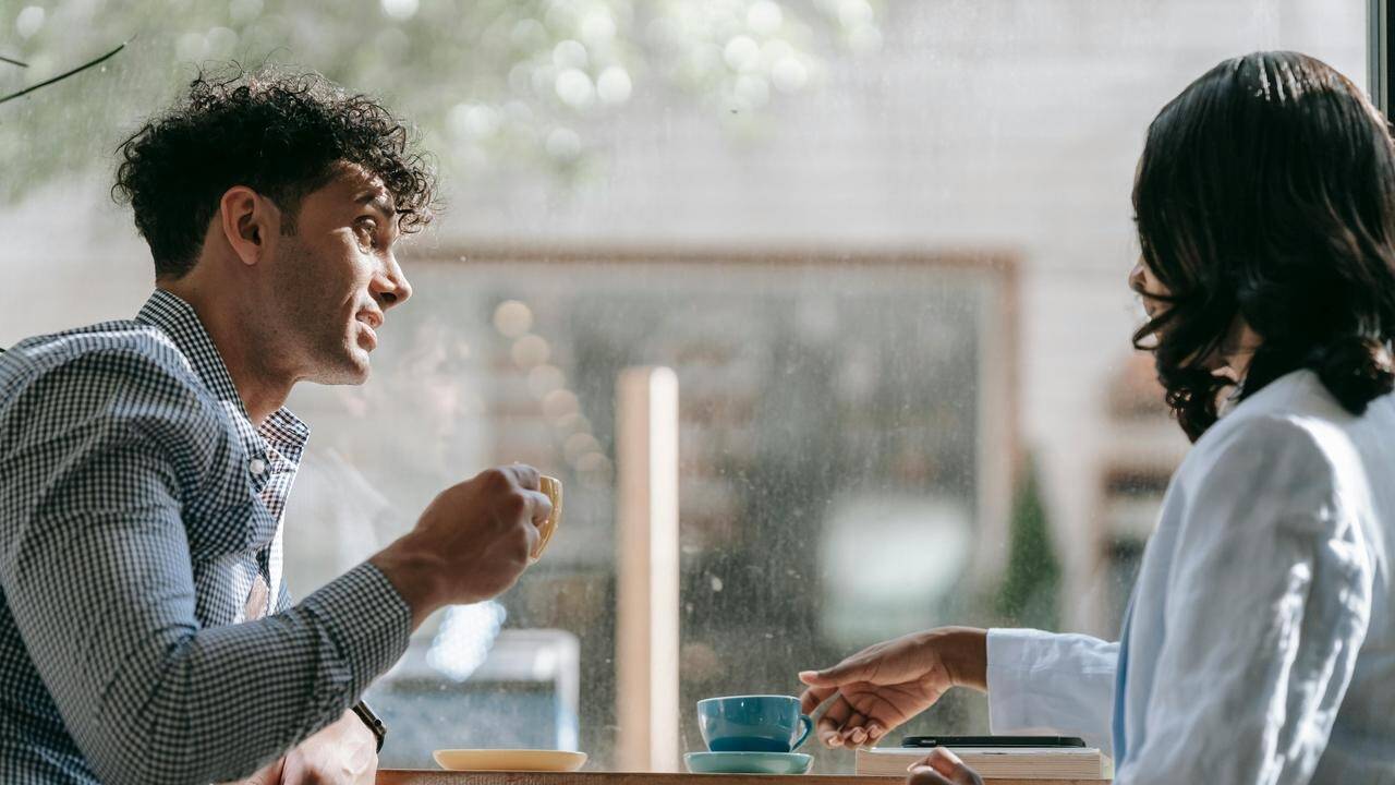 A man and woman sitting by a window, drinking coffee and talking.