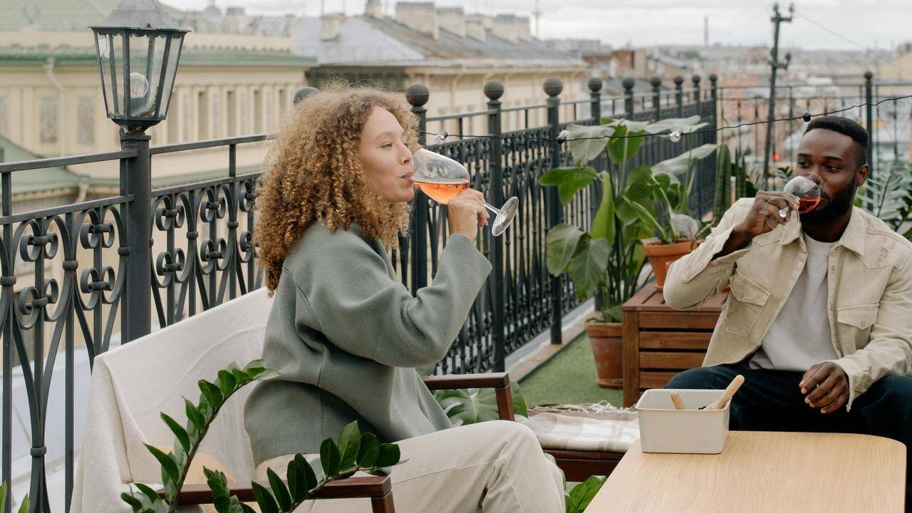 A man and woman sitting on a balcony, drinking wine and relaxing together.