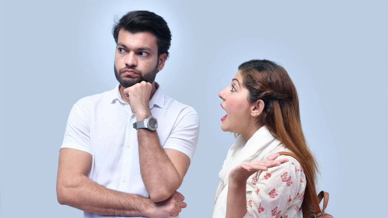 A man rests his chin on his hand while a woman gestures and speaks with mouth open.